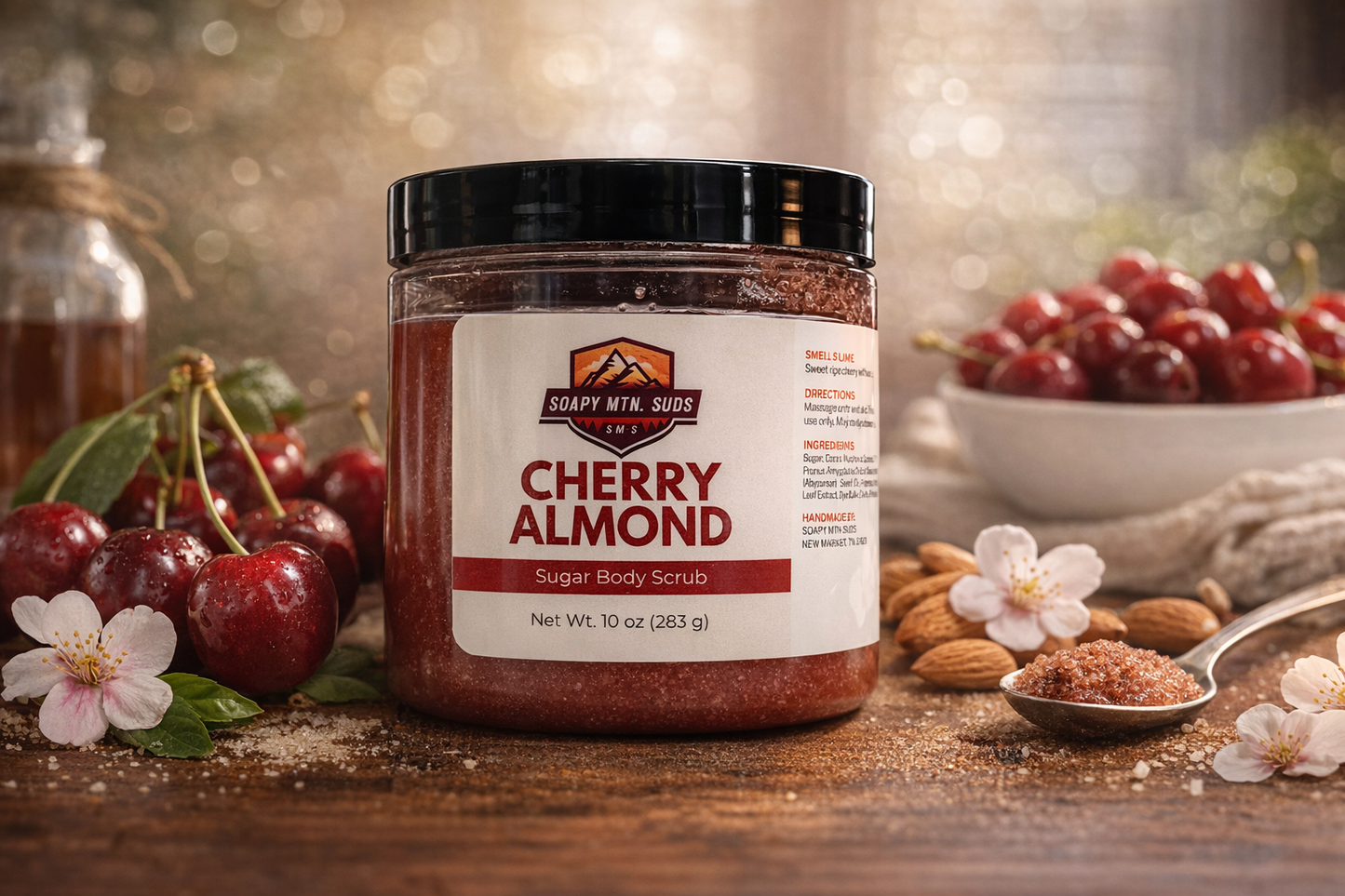 Cherry Almond sugar body scrub by Soapy Mtn Suds, exfoliating handmade scrub with sweet cherry and almond scent in 10 oz jar surrounded by fresh cherries and almonds