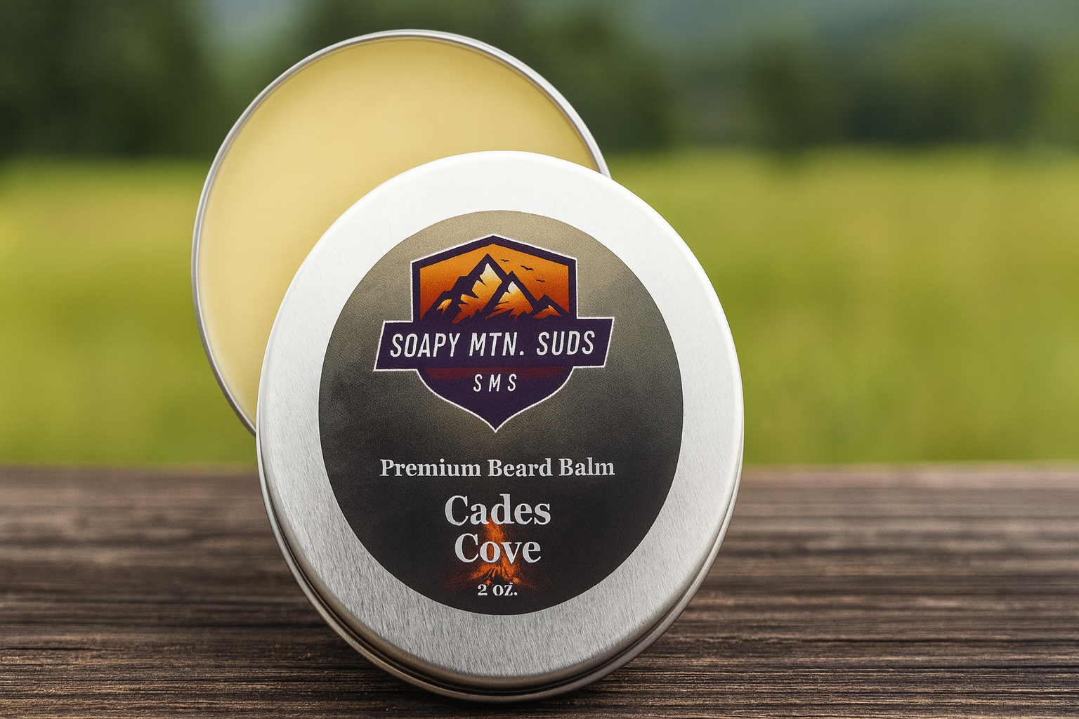 Cades Cove Premium Beard Balm by Soapy Mtn Suds in silver tin on wood table with forest background, handcrafted beard balm offering conditioning hold with warm woodsy masculine scent inspired by the Smoky Mountains