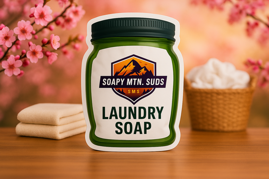 Soapy Mtn Suds Cherry Almond Type Laundry Soap in green mason jar bag, sweet nutty cherry almond scent with folded towels, pink blossoms, and cozy spring-inspired background.