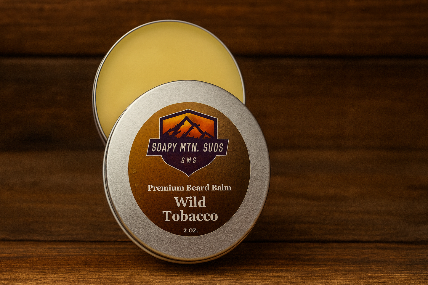 Wild Tobacco Premium Beard Balm by Soapy Mtn Suds — 2 oz handcrafted beard balm tin with warm, earthy tobacco, spice, and vanilla notes on rustic wood background.